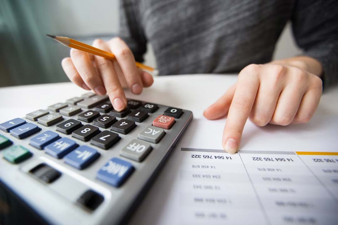 Mãos de uma empresária utilizando uma calculadora para alimentar uma planilha com números da empresa