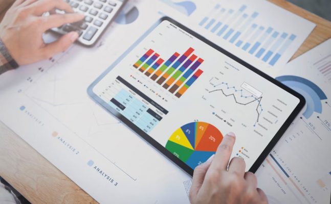 Parte da mão de um profissional de contabilidade apontando para a tela de um tablet que contém um dashboard com números e gráficos contábeis