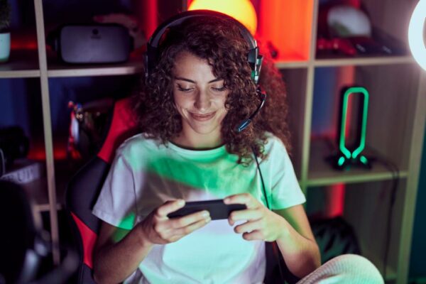 jovem-bela-mulher-hispanica-streamer-jogando-videogame-usando-smartphone-na-sala-de-jogos