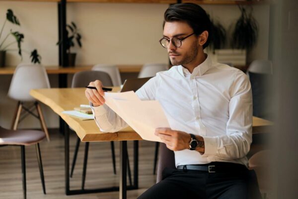 jovem-empresario-serio-em-oculos-trabalhando-pensativamente-com-papeis-no-escritorio-moderno