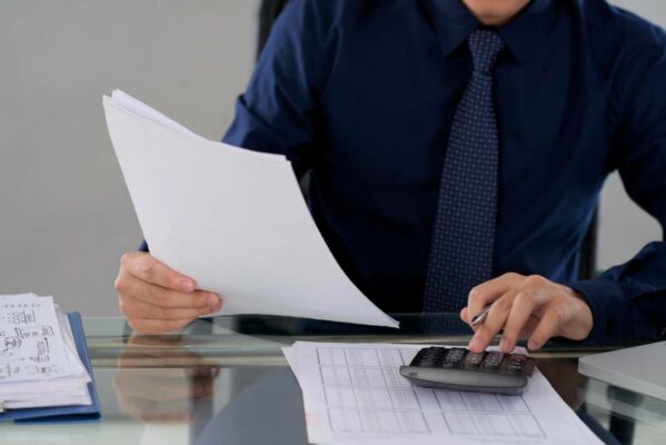 homem segurando folha de papel sentando em uma mesa dentro de um escritorio